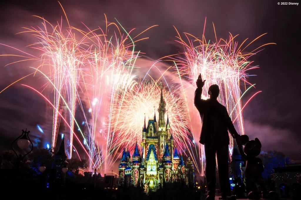 Happily Ever After Cinderella Castle lit up with fireworks in the background and a statue of Mickey and Walt in the foreground