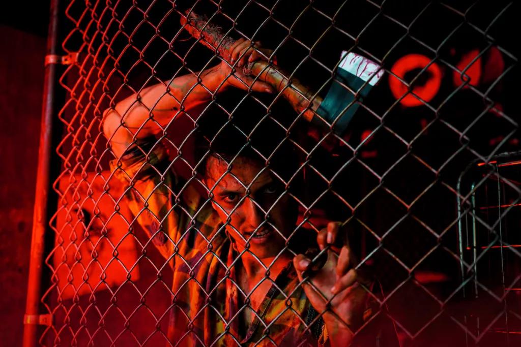 Creek Freaks Unchained A man with an axe leaning up against a chain fence in a dark room lit with red lights