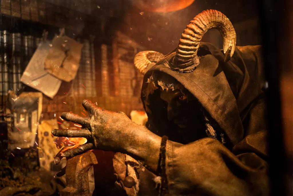 Death's Doors A creature with curved horns and a hooded cloak leaning over a blacksmith's block