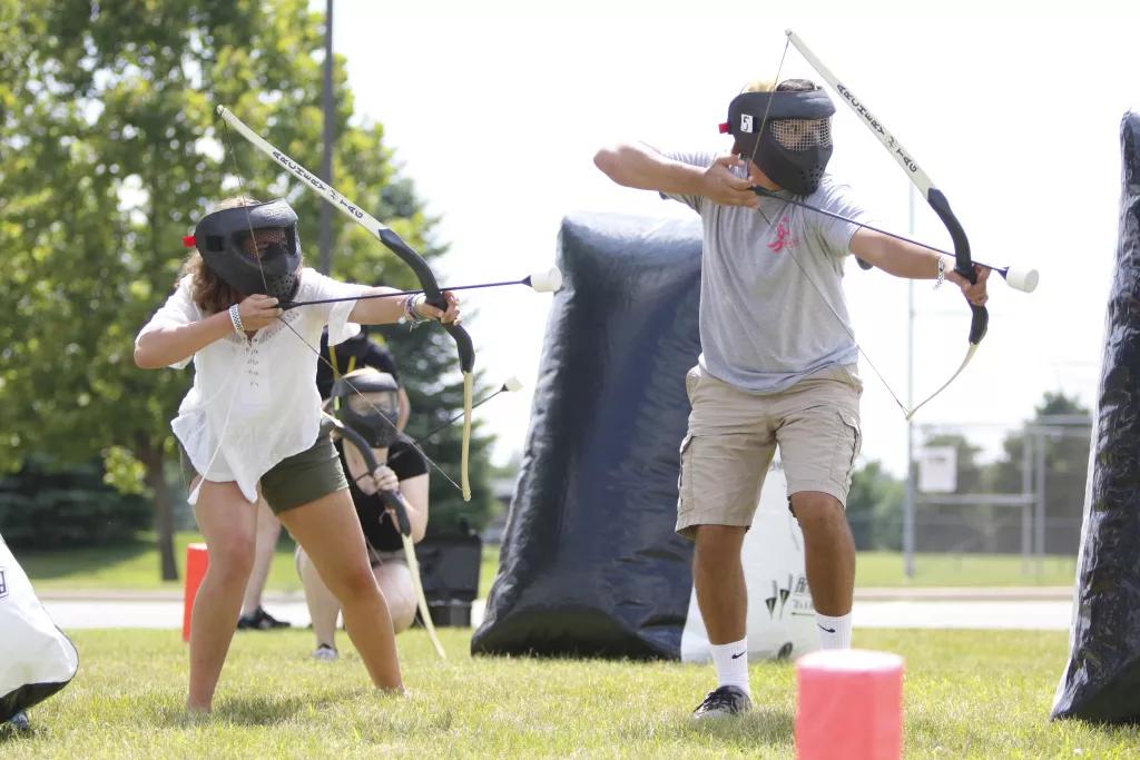 Archery Tag A man and woman wearing helmets and holding bows and arrows playing archery tag