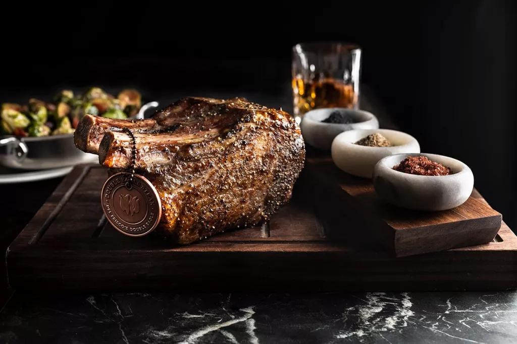 Del Frisco's Double Eagle A cut of cooked steak on a wooden board with pots of spices and a glass of whiskey