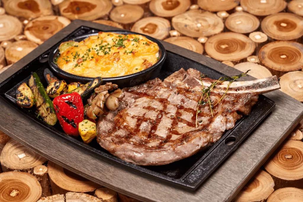 BigFire Ribeye Steak A ribeye steak with mac and cheese and roasted vegetables on a metal tray