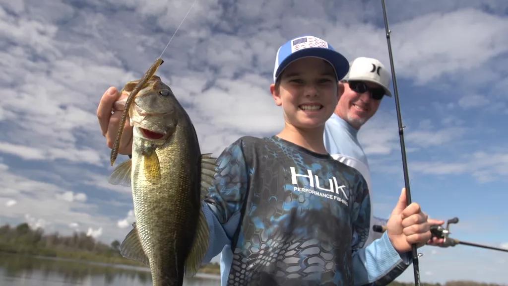 Trophy Bass Fishing A boy holding a fishing rod in one hand and a bass in the other