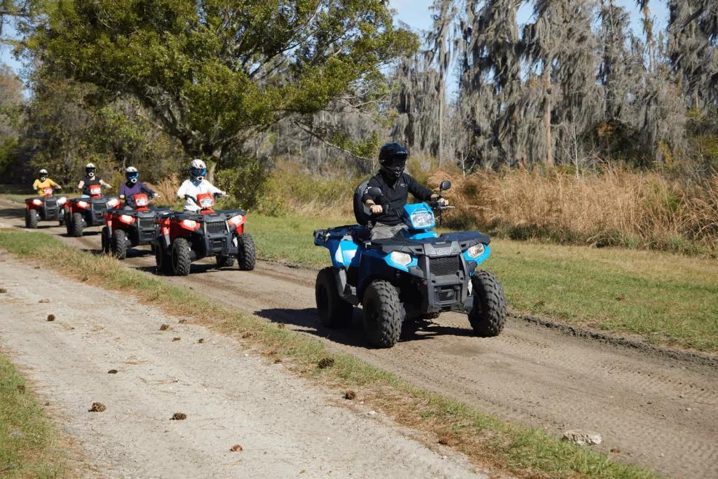 ATV Off-Roading Four people on quad bikes following an instructor in a line along a dirt path surrounded by trees