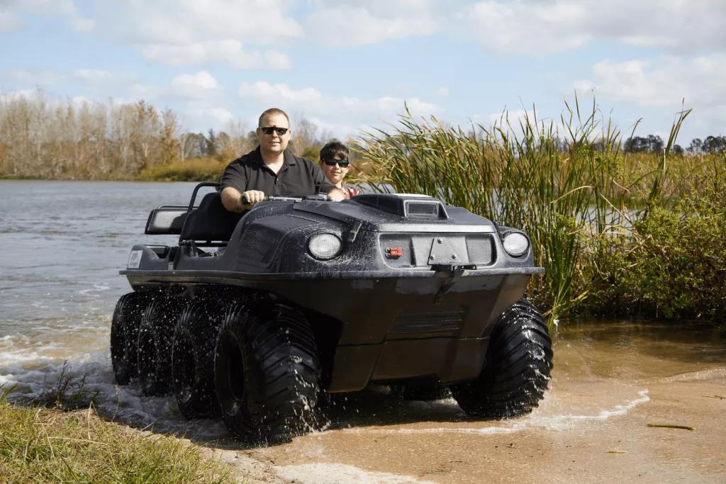 Mucky Ducks A man and boy sitting in a Mucky Duck off road vehicle in front of a lake