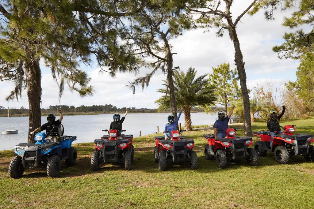 Orlando ATV Experience 5 people riding 4x4 ATVs posing for the camera in front of a lake with one fist in the air