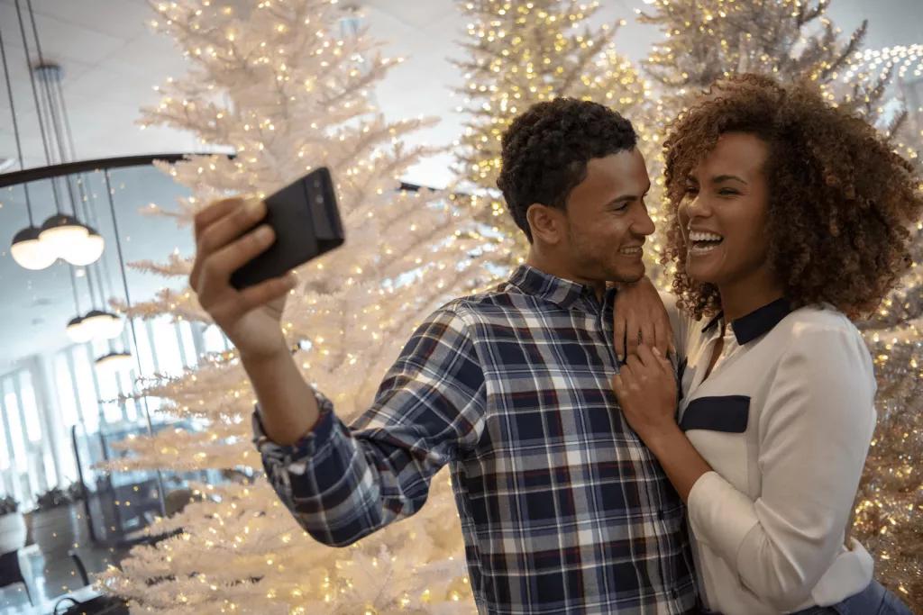 Christmas in Orlando A man and a woman smiling while taking a selfie in front of a lit up Christmas tree