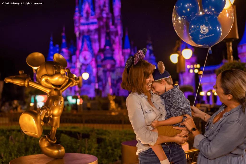 After Hours at Magic Kingdom Park Two women, one holding a small child with a balloon in his hand, standing next to a statue of Mickey Mouse