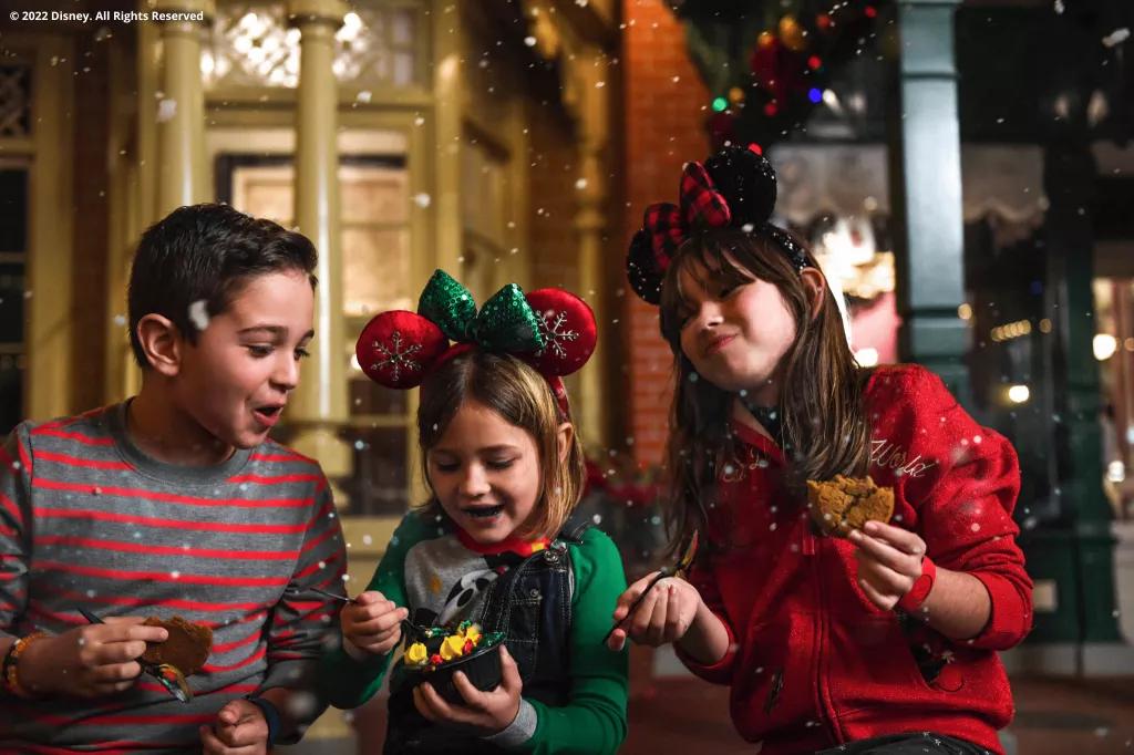 Three children wearing red and green sat on Main Street USA eating Christmas themed treats