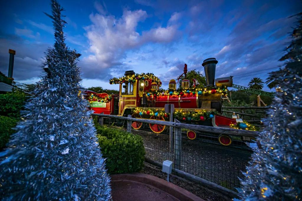 Holly Jolly Express A train decorated with colourful tinsel on a track next to some silver Christmas trees