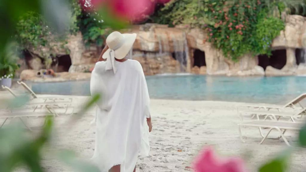 Discovery Cove A woman in a straw hat and beach cover-up walking along an empty beach