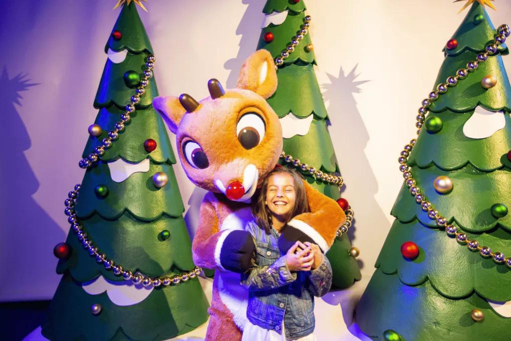 Rudolph's Winter Wonderland A child being hugged by someone in a Rudolph costume, with cartoon Christmas trees behind them