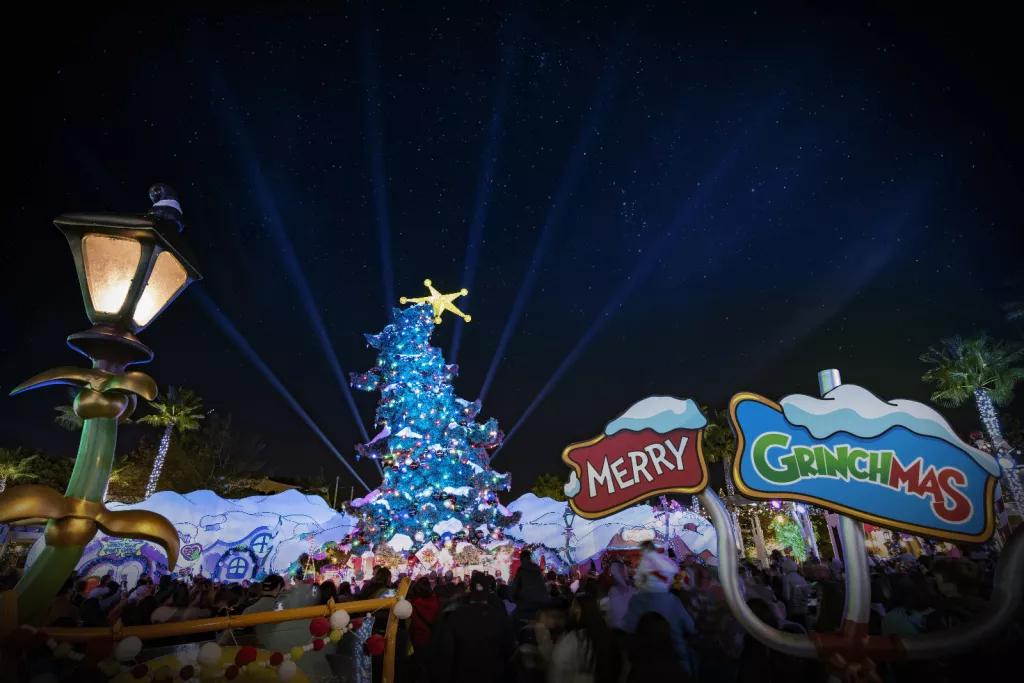 Grinchmas A sign reading Merry Grinchmas in front of a tall Christmas tree that curves at the top