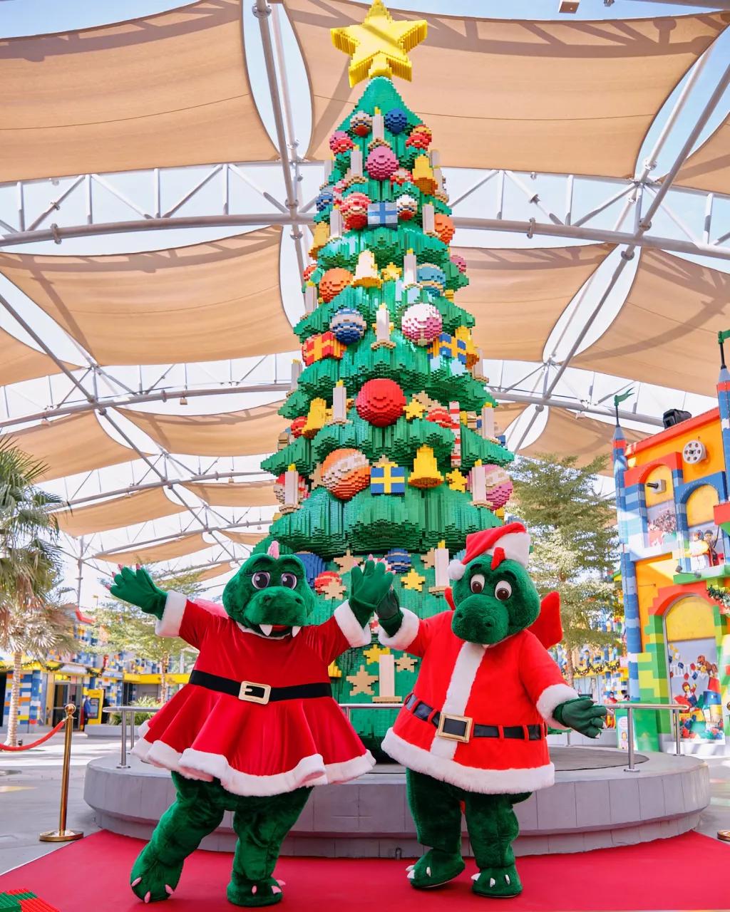 Festive Bricktacular at Legoland Dubai Two crocodile characters dressed as Santa and Mrs Claus standing in front of a LEGO Christmas tree