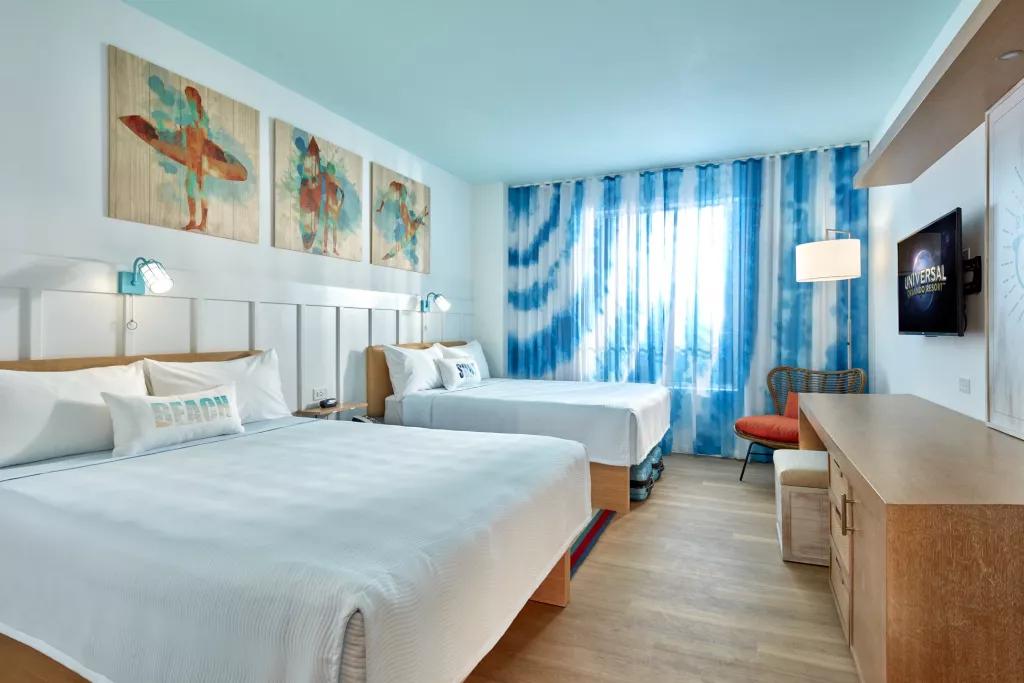 A Standard Room at Universal's Surfside Inn and Suites A beach themed hotel room with two double beds facing a desk, chair and wall-mounted TV