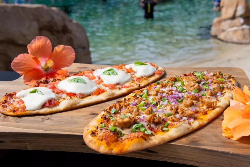 Pizzas at Hibiscus Hideaway Two long flatbread pizzas on a wooden board in front of a the clear blue waters of the beach