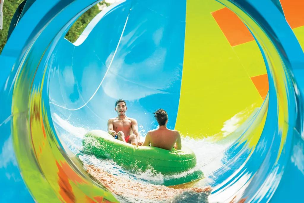 KareKare Curl at Aquatica Two men in swimming costumes riding in a rubber raft down a multicoloured waterslide