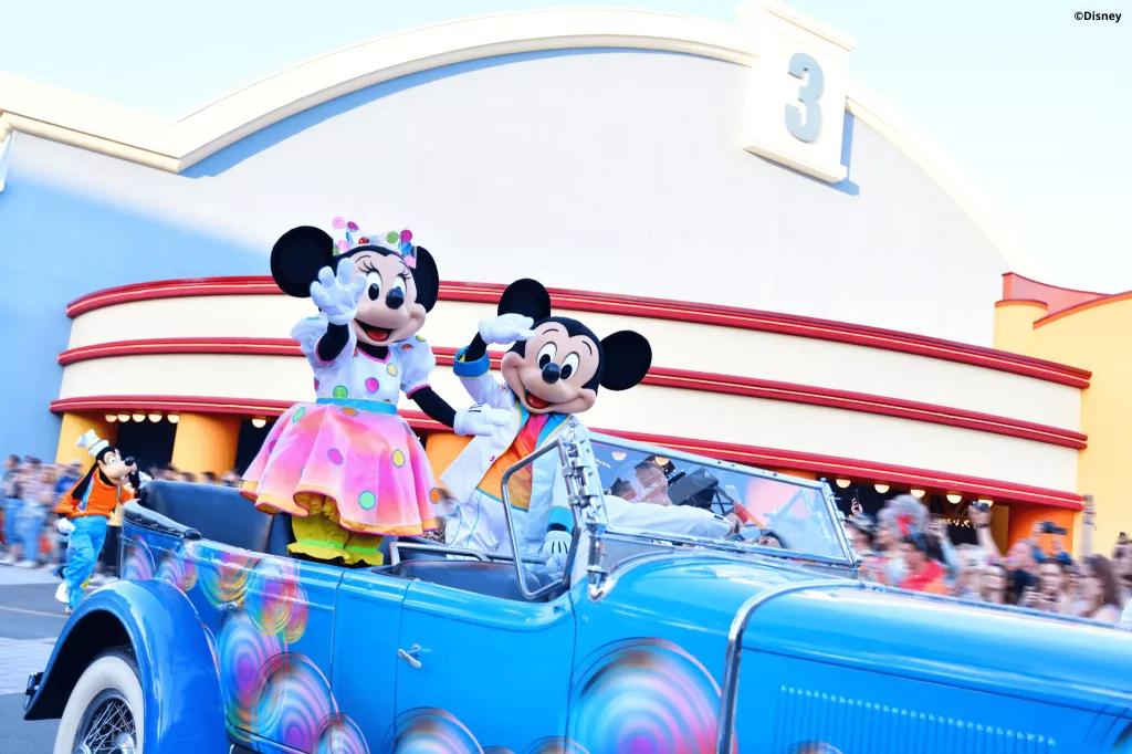 Disney Colourful Pride Parade Mickey and Minnie Mouse wearing rainbow outfits waving at a crowd from a convertible car