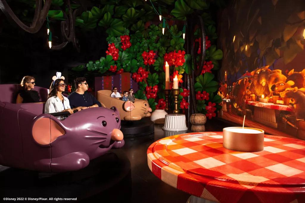 Remy's Ratatouille Adventure at EPCOT Guests in ride vehicles shaped like rats looking at a large screen and wearing 3D glasses. They are surrounded by larger than life objects