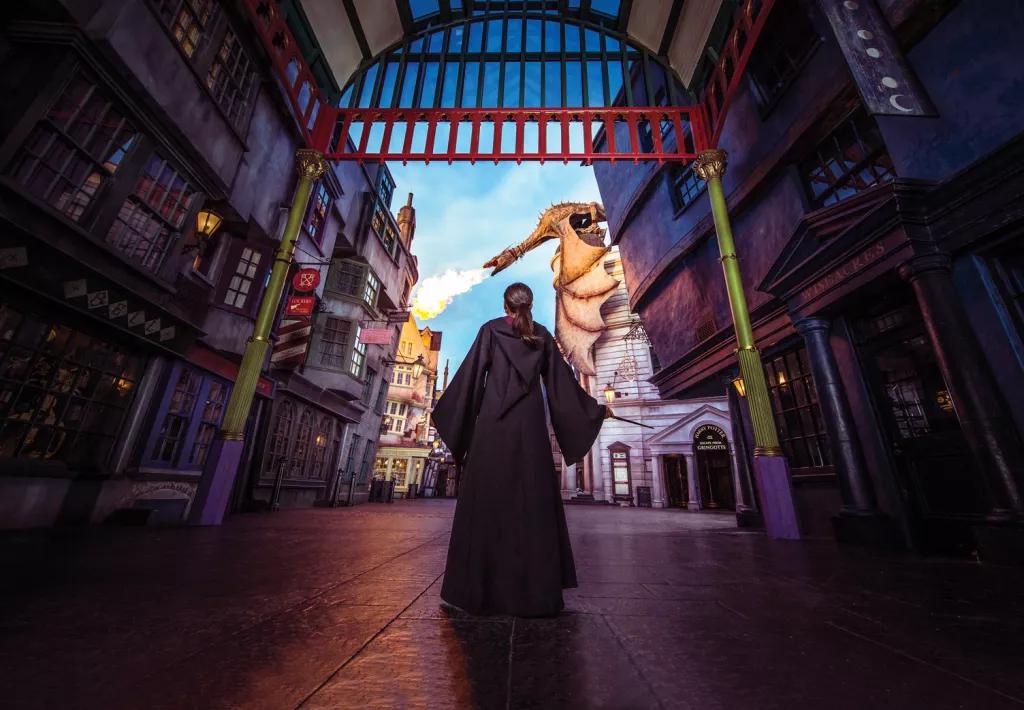 Diagon Alley at Universal Studios Florida A girl in Diagon Alley wearing wizard robes and holding a wand, looking up to a fire breathing dragon on the top of a building