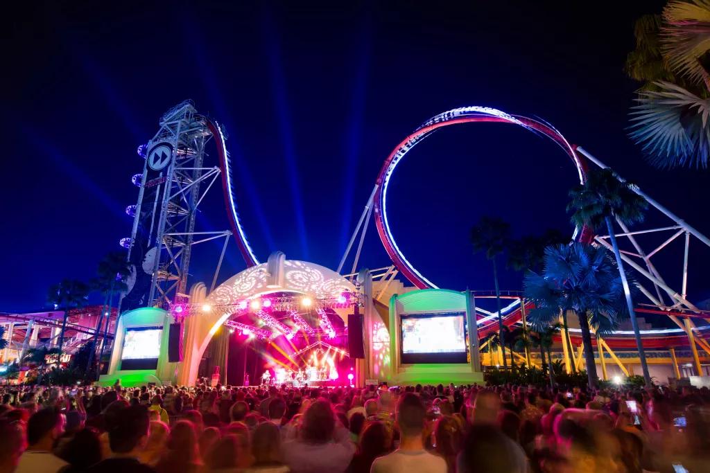 Mardi Gras Concert Performances A crowd of people watching a musical act on a stage in front of a large rollercoaster