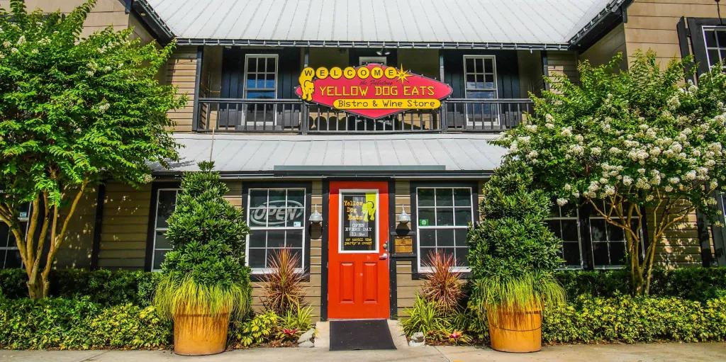 Yellow Dog Eats The exterior of a restaurant with a red front door and a sign reading Welcome to Yellow Dog Eats above it