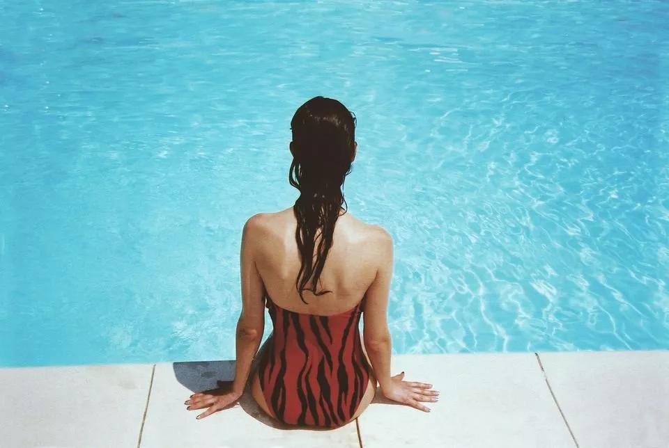Swimming Costume A woman wearing a swimming costume sat on the edge of a pool with her feet in the water