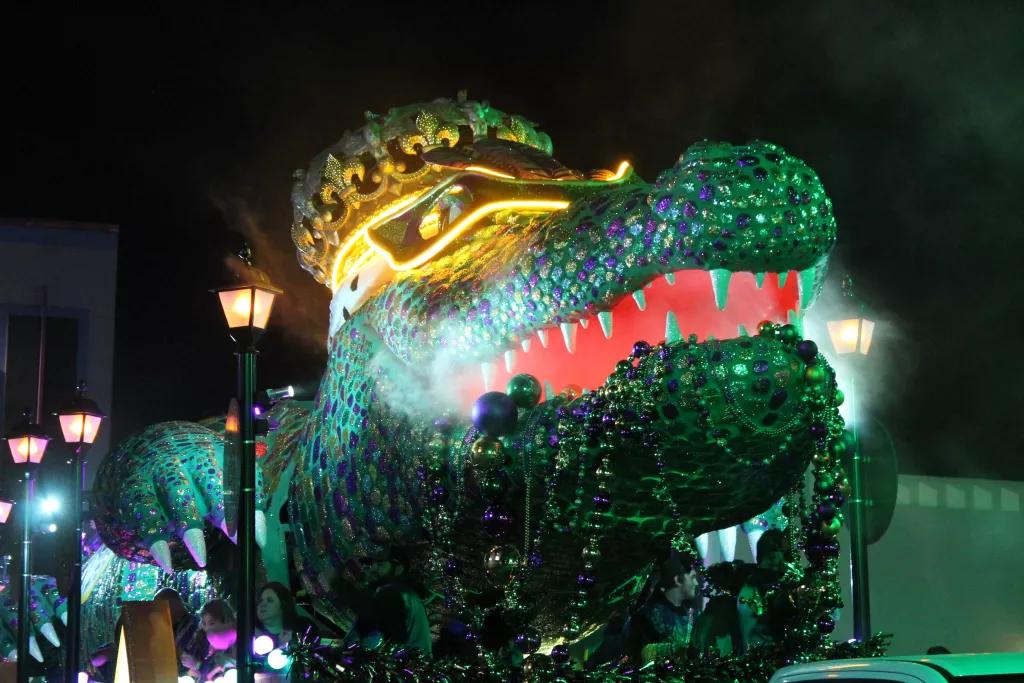 Mardi Gras Parade Floats A large parade float shaped like an alligator wearing a crown and holding strings of beads in its mouth