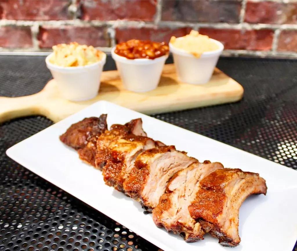 This Little Piggy Barbecue A plate of barbecued meat in front of a range of sides including baked beans and mac & cheese