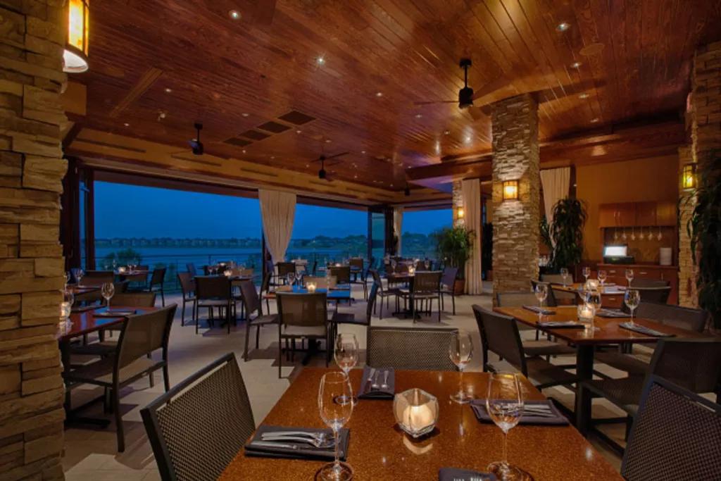 Seasons 52 A restaurant dining room full of empty tables in front of a large window looking out over a body of water