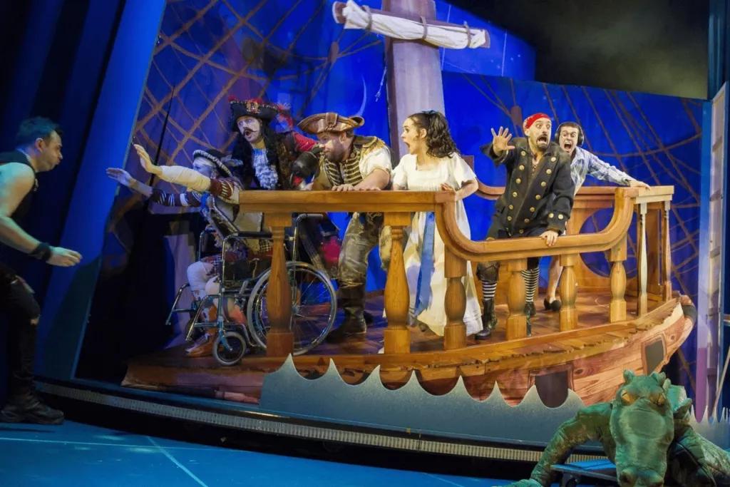 Peter Pan Goes Wrong Actors playing Wendy, Captain Hook and other pirates from Peter Pan on a stage set to look like a pirate ship