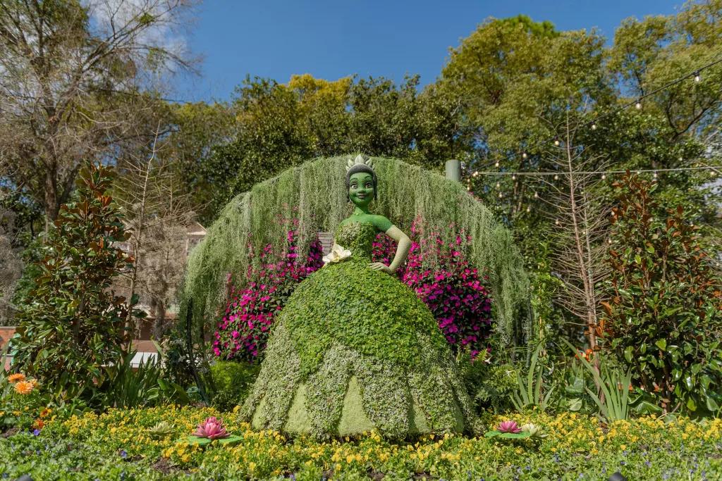 Princess Tiana Topiary A life-size topiary designed to look like Princess Tiana in front of a wall of plants and flowers