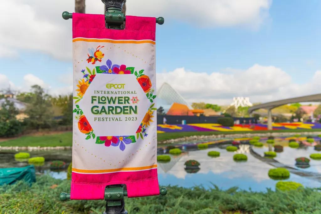 EPCOT Flower and Garden Festival A sign reading EPCOT Flower and Garden Festival in front of a blue sky and flower beds