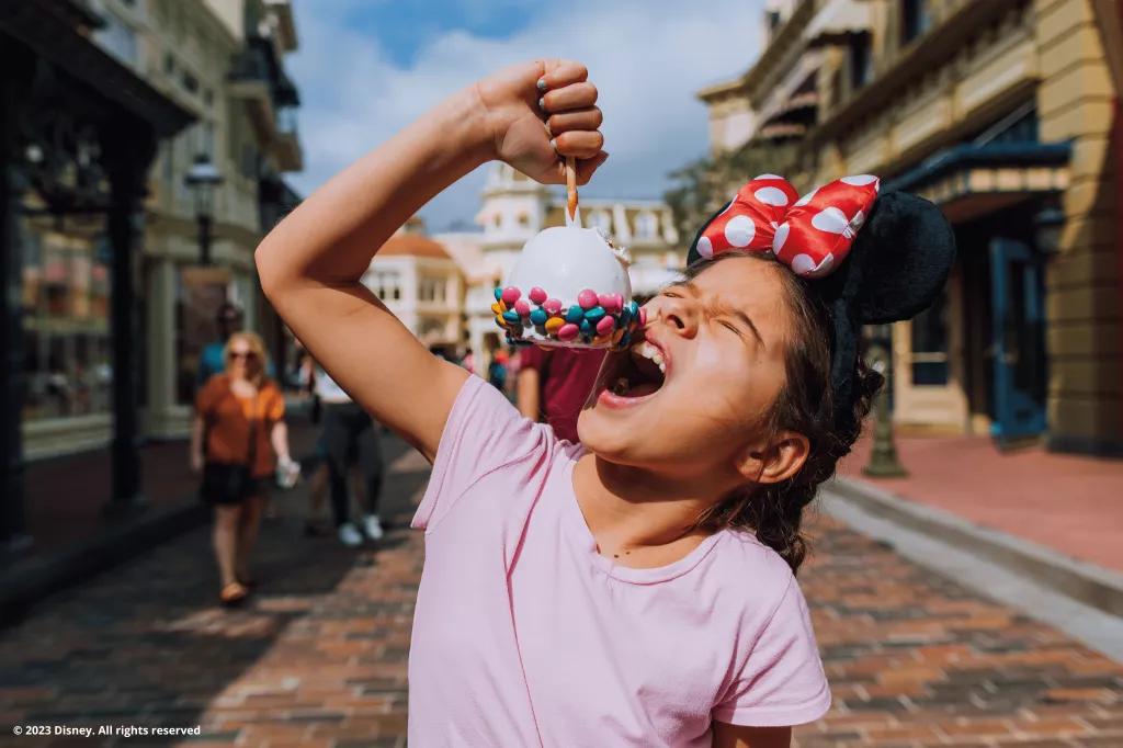 Snacks at Walt Disney World Resort in Florida A young girl wearing a pink tshirt and Minnie Mouse ears biting into a large candy apple