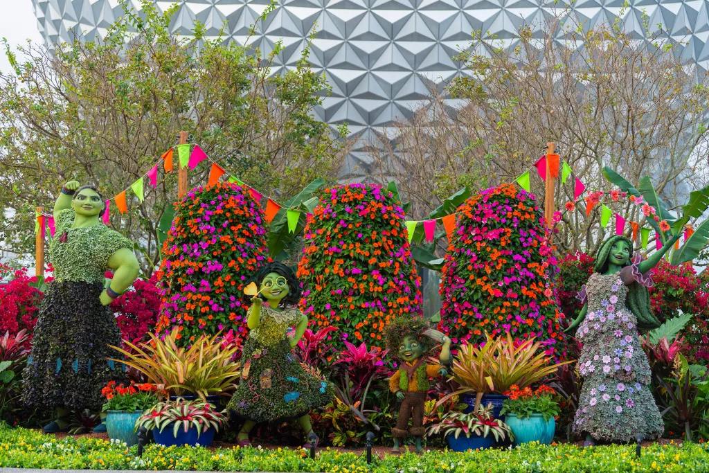 International Flower and Garden Festival Topiaries shaped like characters from Encanto in front of colourful flowers and hedges with Spaceship Earth in the background