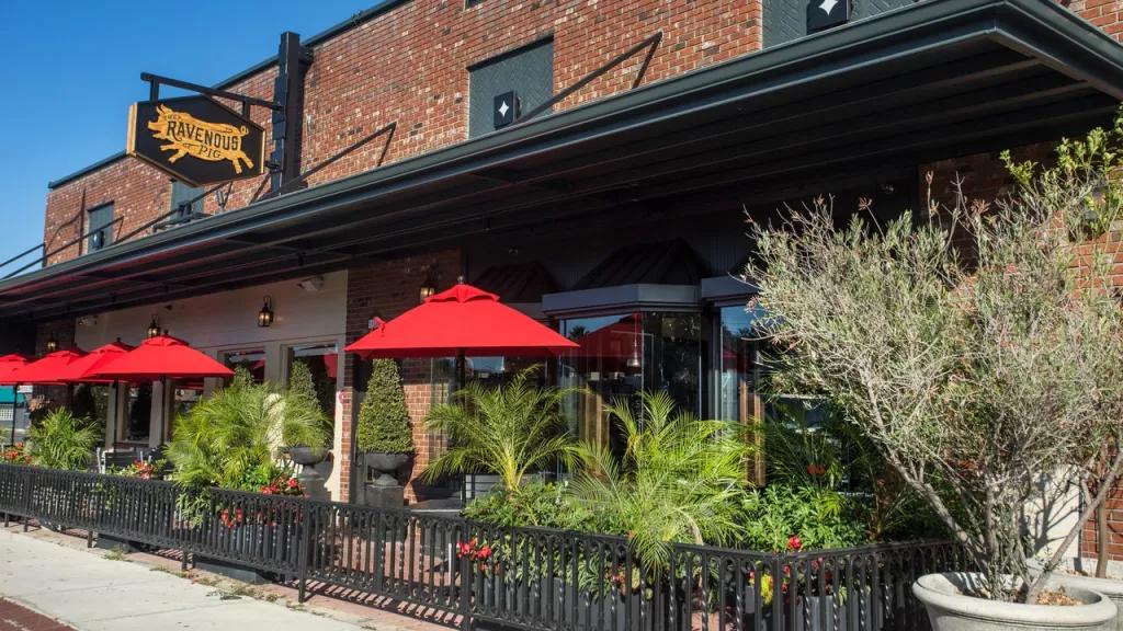 The Ravenous Pig in Orlando The exterior of a brick building with a patio covered by red umbrellas