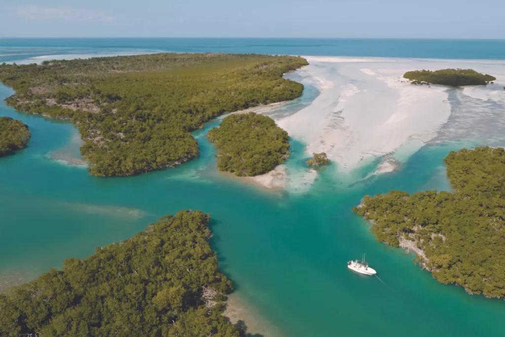 The Lower Keys An aerial view of a boat sailing through the teal waters between the sandy islands of the Florida Keys