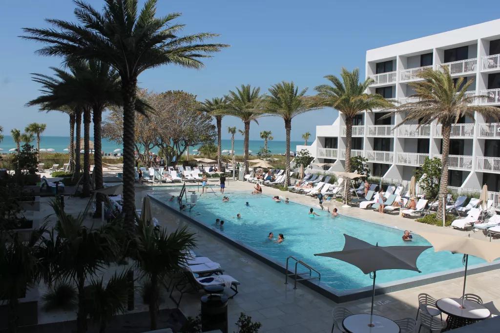 Zota Beach Resort A hotel pool surrounded by palm trees and sun loungers, looking out to the ocean in the background