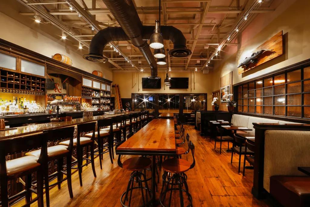 The Ravenous Pig The interior of a restaurant with wooden table and floors and a long bar with stools along one side