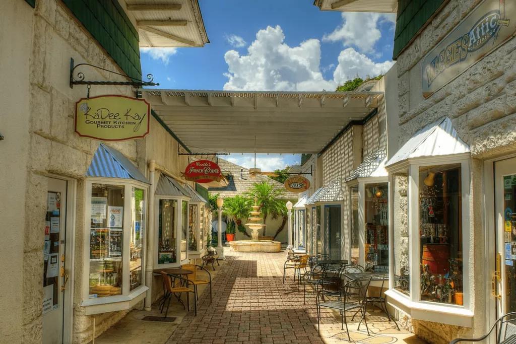Mount Dora A covered walkway lined with shops with tables and chairs outside, leading to a fountain at the end