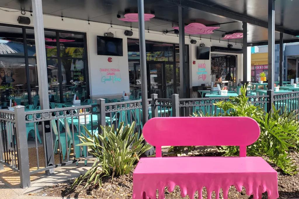 Outdoor Patio Seating A covered outdoor patio at a restaurant with blue tables and chairs and a bright pink bench in the foreground