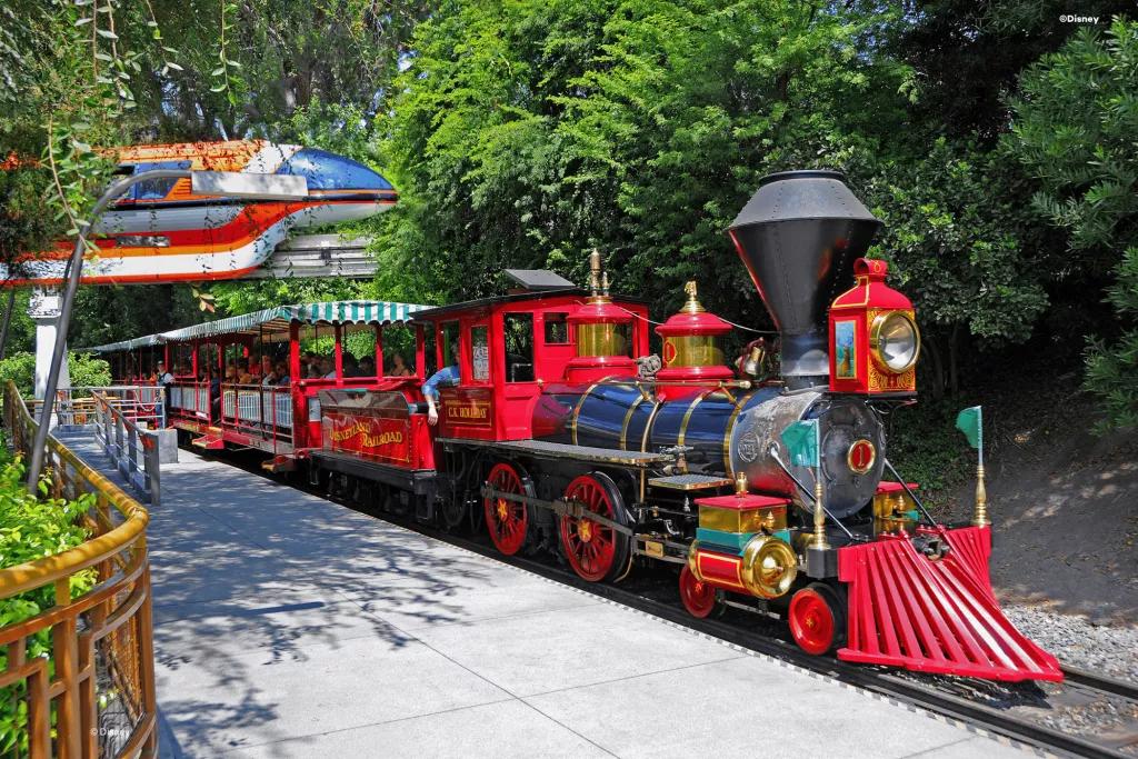 Disneyland Railroad A classic steam train with red accents waiting in a station with a monorail going past in the background