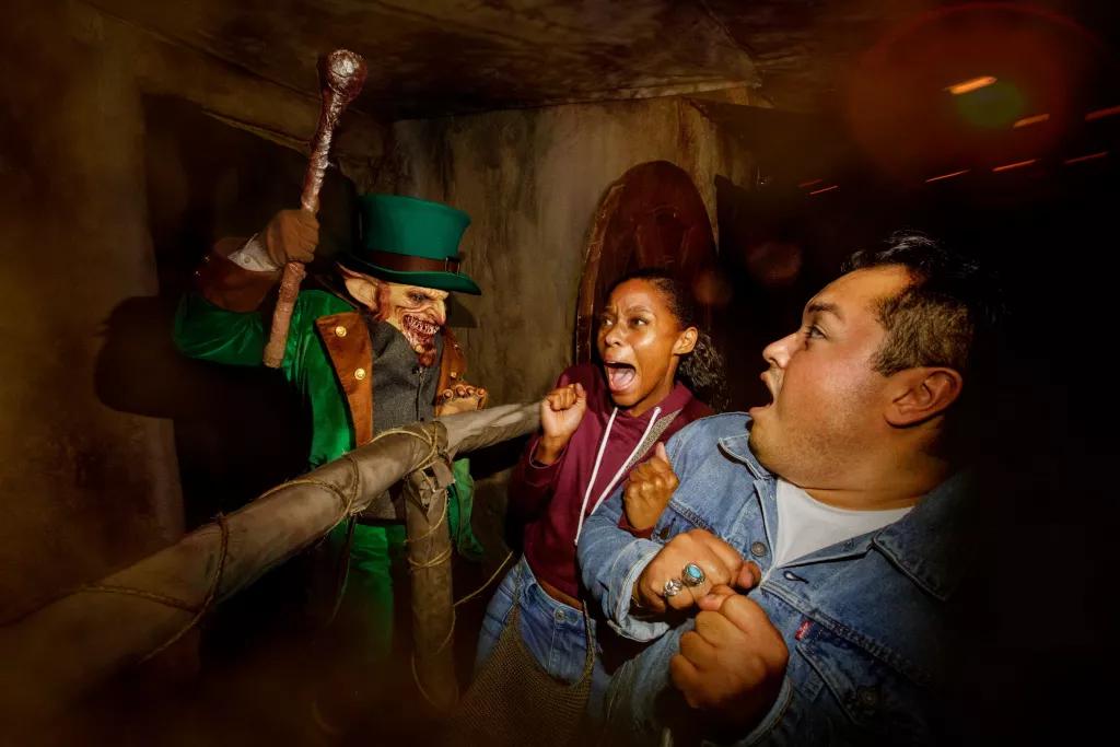 Scare Actors at Halloween Horror Nights A scare actor dressed as a leprechaun jumping out at a man and a woman who are both screaming