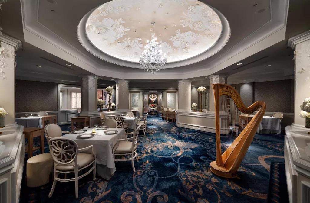 Victoria and Albert's at Walt Disney World Resort The interior of a restaurant with a chandelier hanging from the ceiling and a harp next to some white tables and chairs
