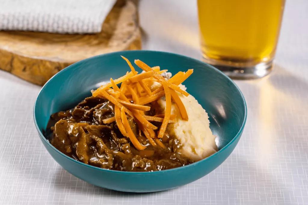 Sauerbrauten and Mashed Potato A bowl of stew and mashed potatoes on a table with a pint of beer