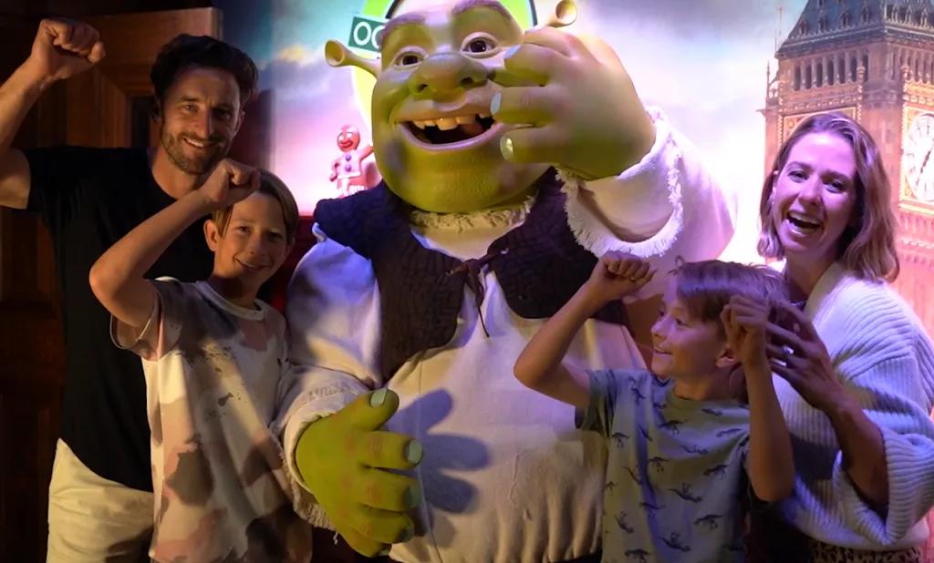 Familie lacht in Shrek's Adventure Eine lachende Familie steht mit der Filmfigur Shrek in Shrek's Adventure