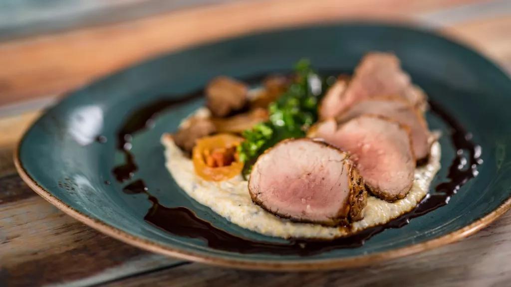 Pork Tenderloin at California Grill A plate with slices of pork and vegetables on top of grits