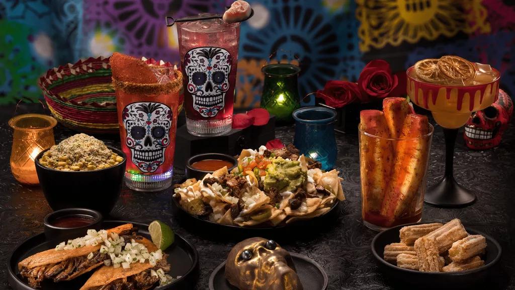 USH Halloween Horror Nights Food A table full of food including nachos, tacos, churros, candy skull cocktails and a cake shaped like a skull