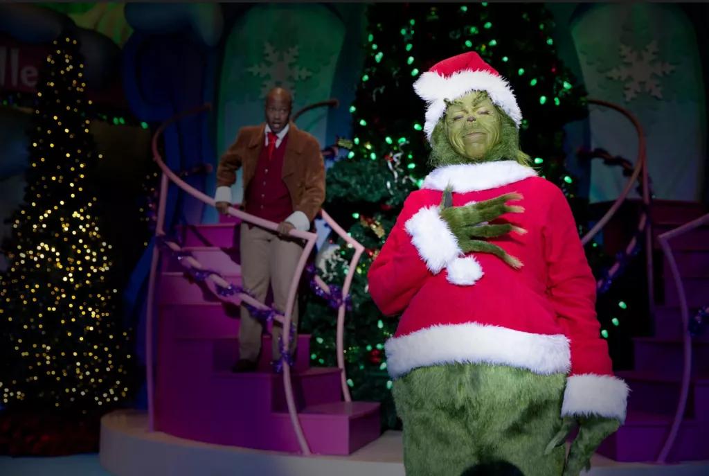 Grinchmas Who-liday Spectacular The Grinch dressed as Santa standing with his hand on his heart
