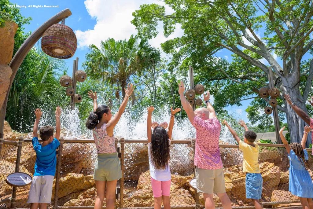 Journey of Water, Inspired by Moana A family standing in a line facing away from the camera holding their arms up to control the water fountains in front of them
